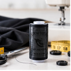 Carrete de hilo negro en mesa de costura