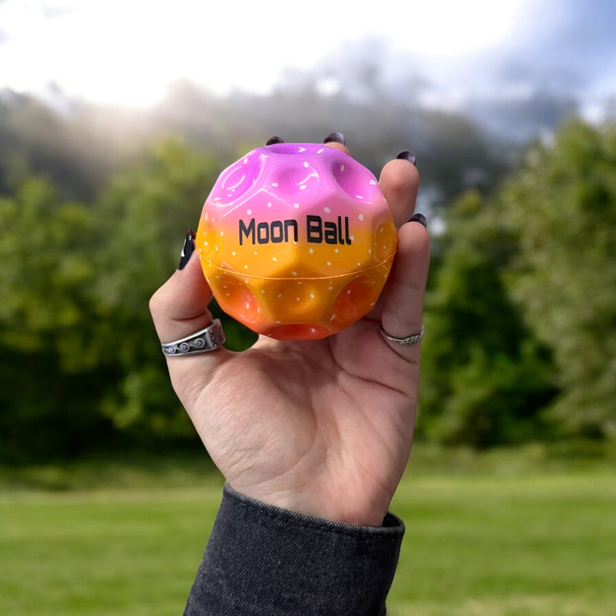 Bola Moon Ball morada y naranja sostenida en una mano al aire libre