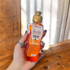 Botella de aceite corporal Sativa naranja de 100 ml sostenida en la mano
