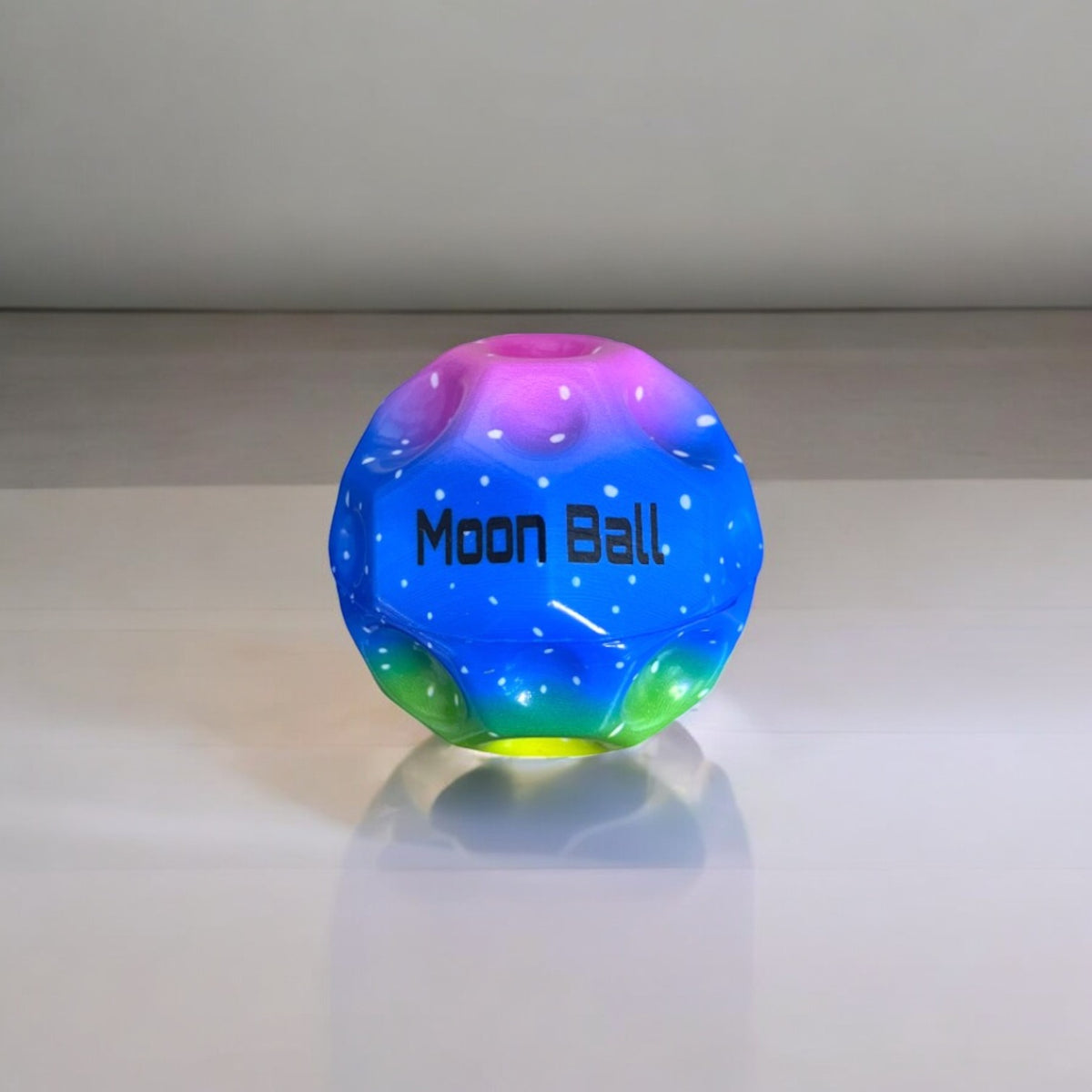 Bola de goma Moon Ball azul y multicolor de 7 cm sobre una mesa
