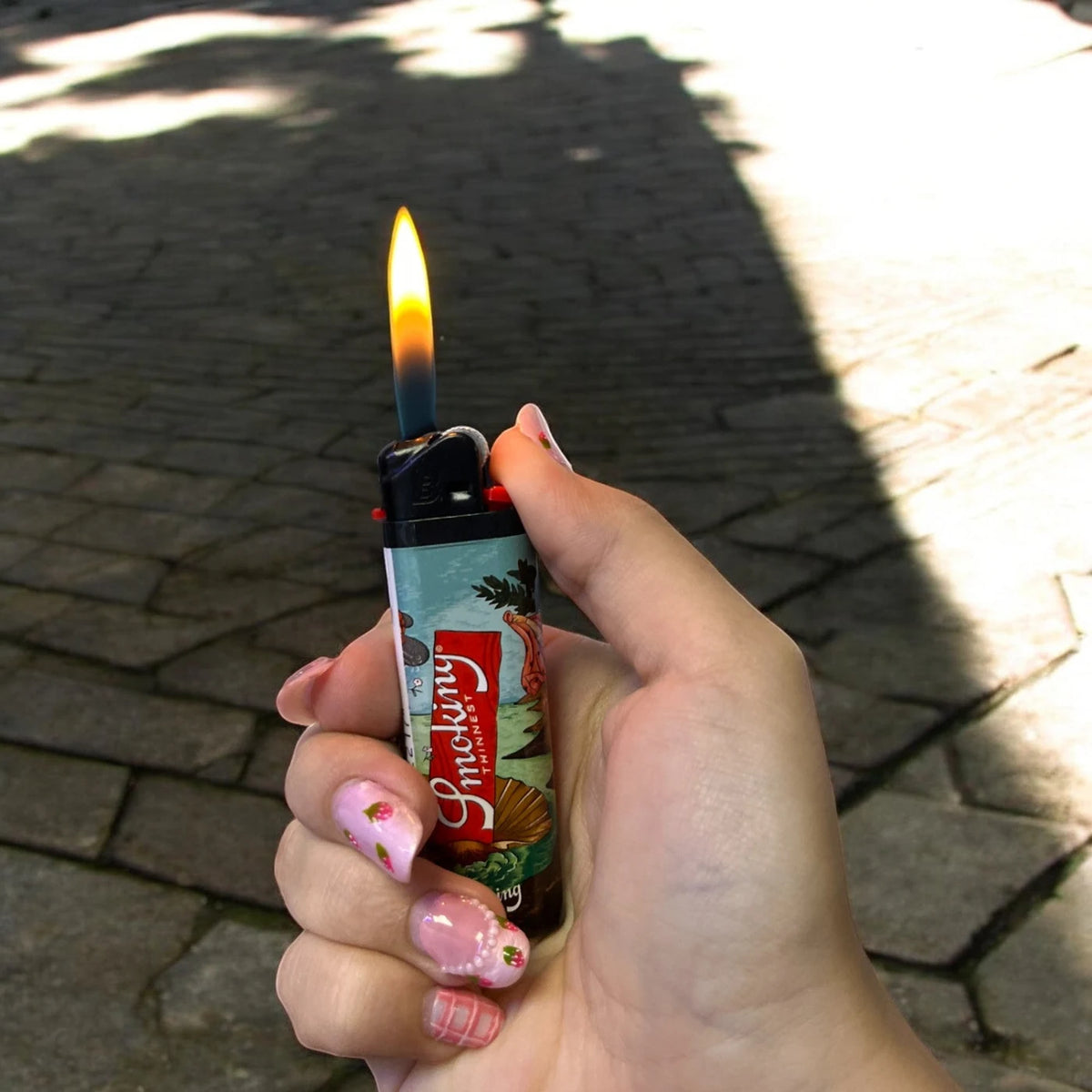 Encendedor Smoking Artist Collection encendido en una mano, con llama visible y carcasa ilustrada.