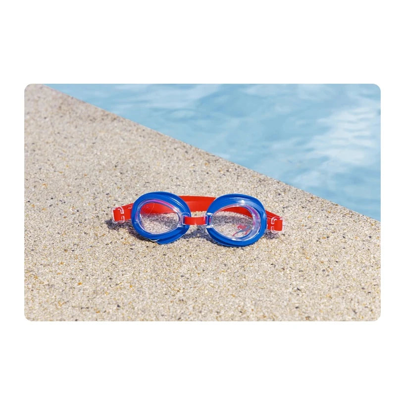 Gafas de natación azules y rojas sobre arena junto a una piscina; el diseño Spider-Man no se distingue.