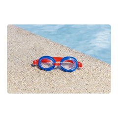 Gafas de natación azules y rojas sobre arena junto a una piscina; el diseño Spider-Man no se distingue.