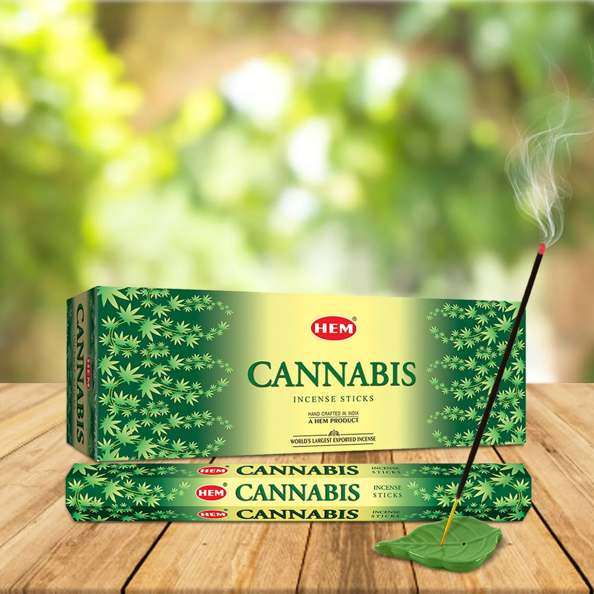 Incienso HEM Cannabis Hexa encendido en soporte de hoja, junto a la caja y las varillas.