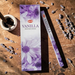 Caja HEM Vanilla con su envase alargado; las flores de lavanda de la escena son decoración y no identifican el aroma.