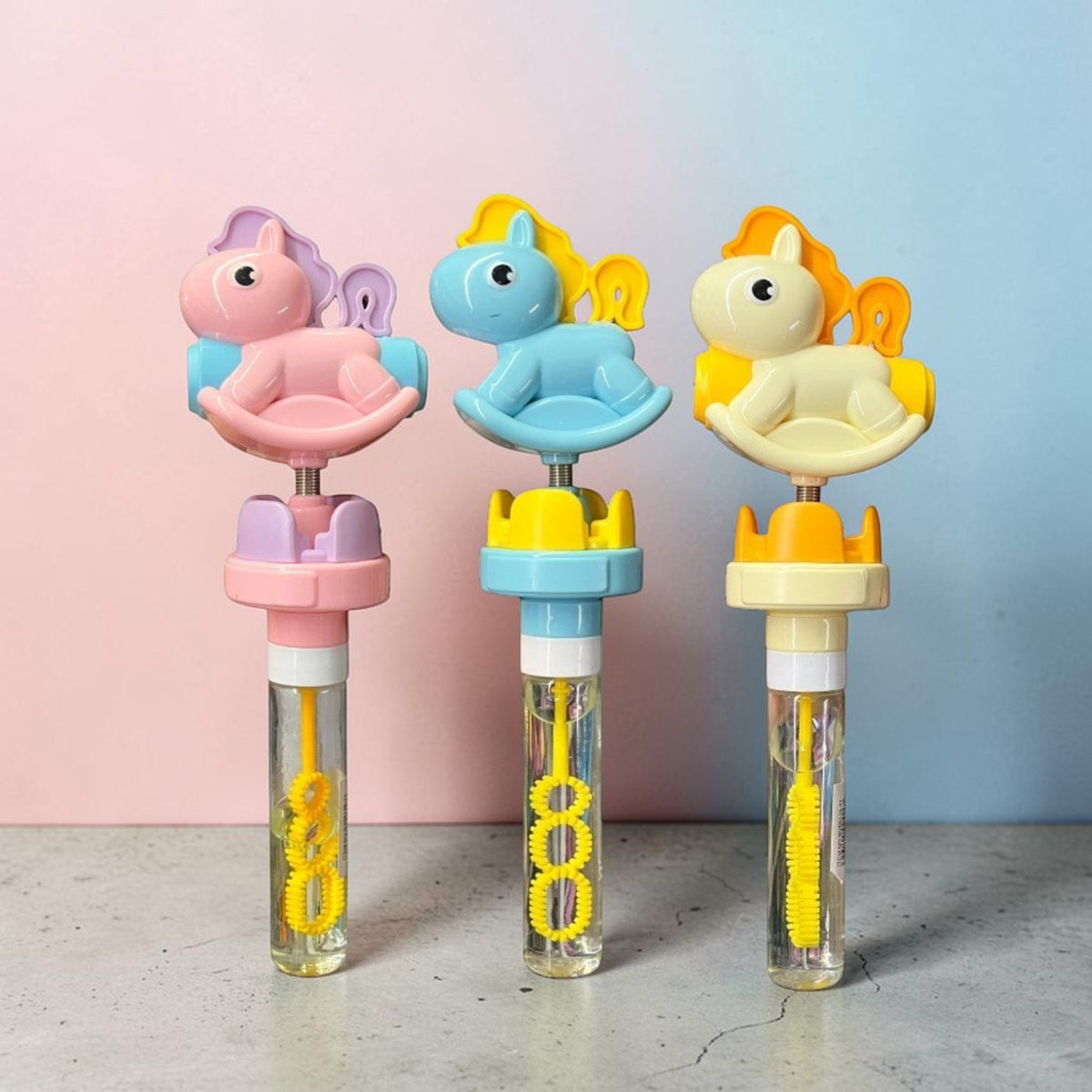 Burbujeadores con figura de pony en rosa, azul y amarillo, cada uno con tubo de solución y aro para burbujas.